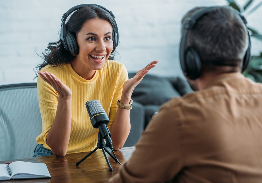 A woman wearing a yellow top and black headphones with a microphone in front of her, engaged in an interview.